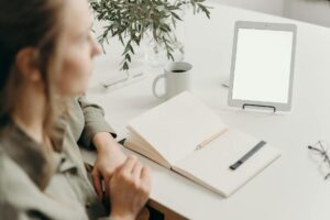 boy in gray jacket sitting beside table with white printer paper and white ceramic mug